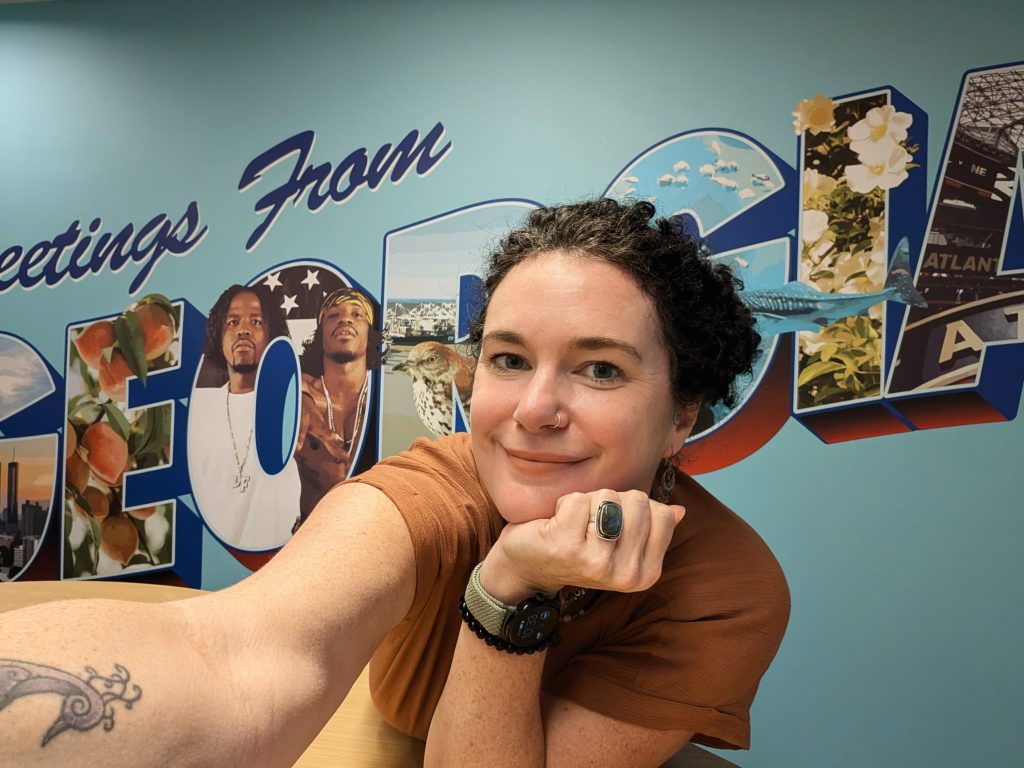 Heather Worthan smiling in front of a Greetings from Georgia mural